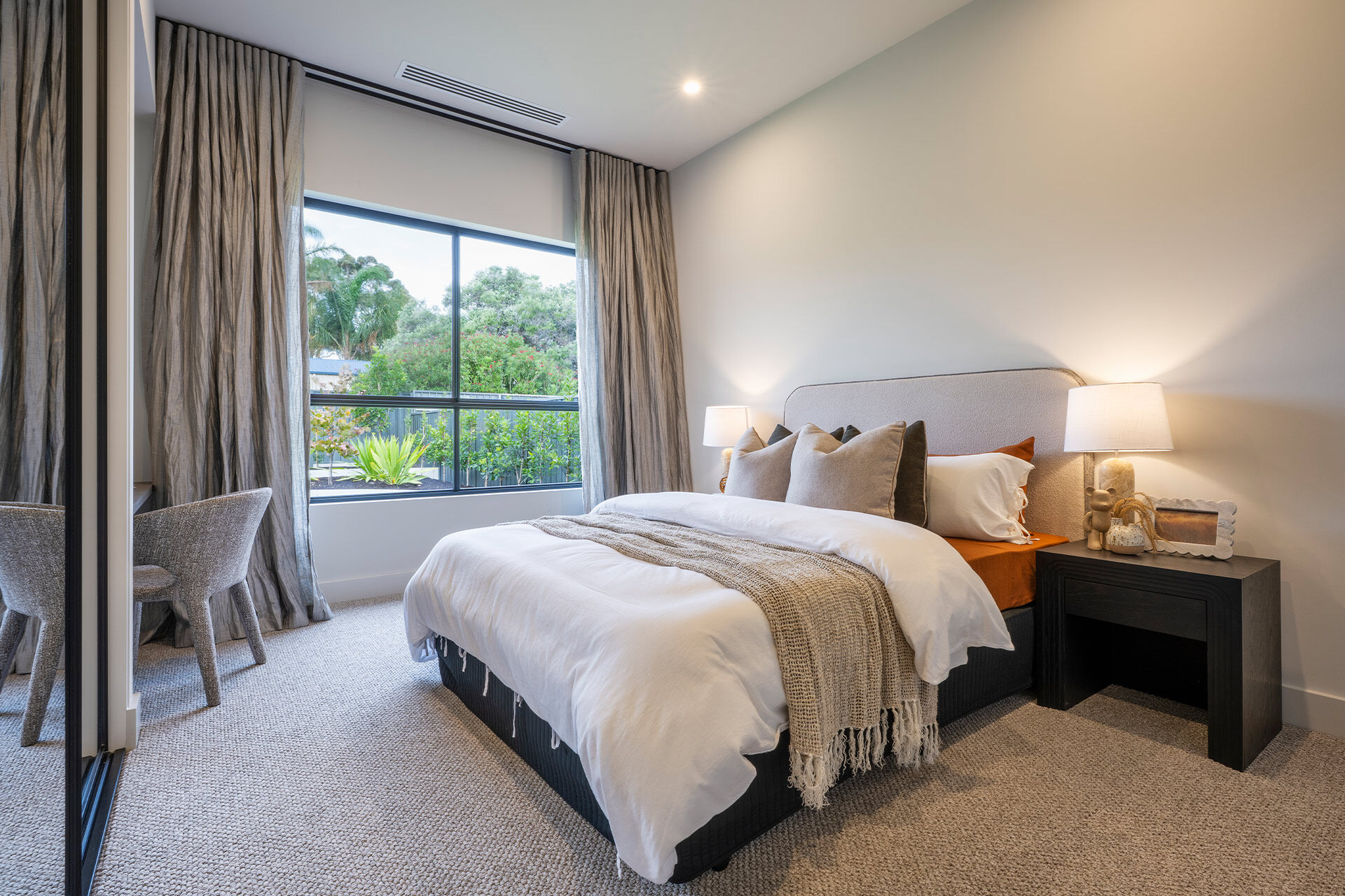 Bedroom with white and beige linen and curtains open to the view of the backyard