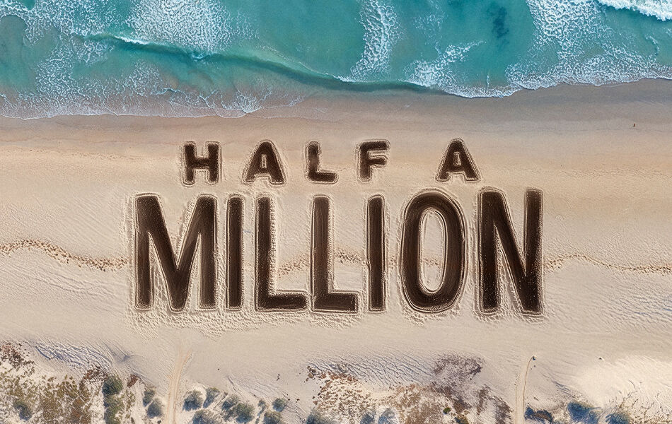 Ariel view beach sand and waves with Half A Million written in the sand waves crashing
