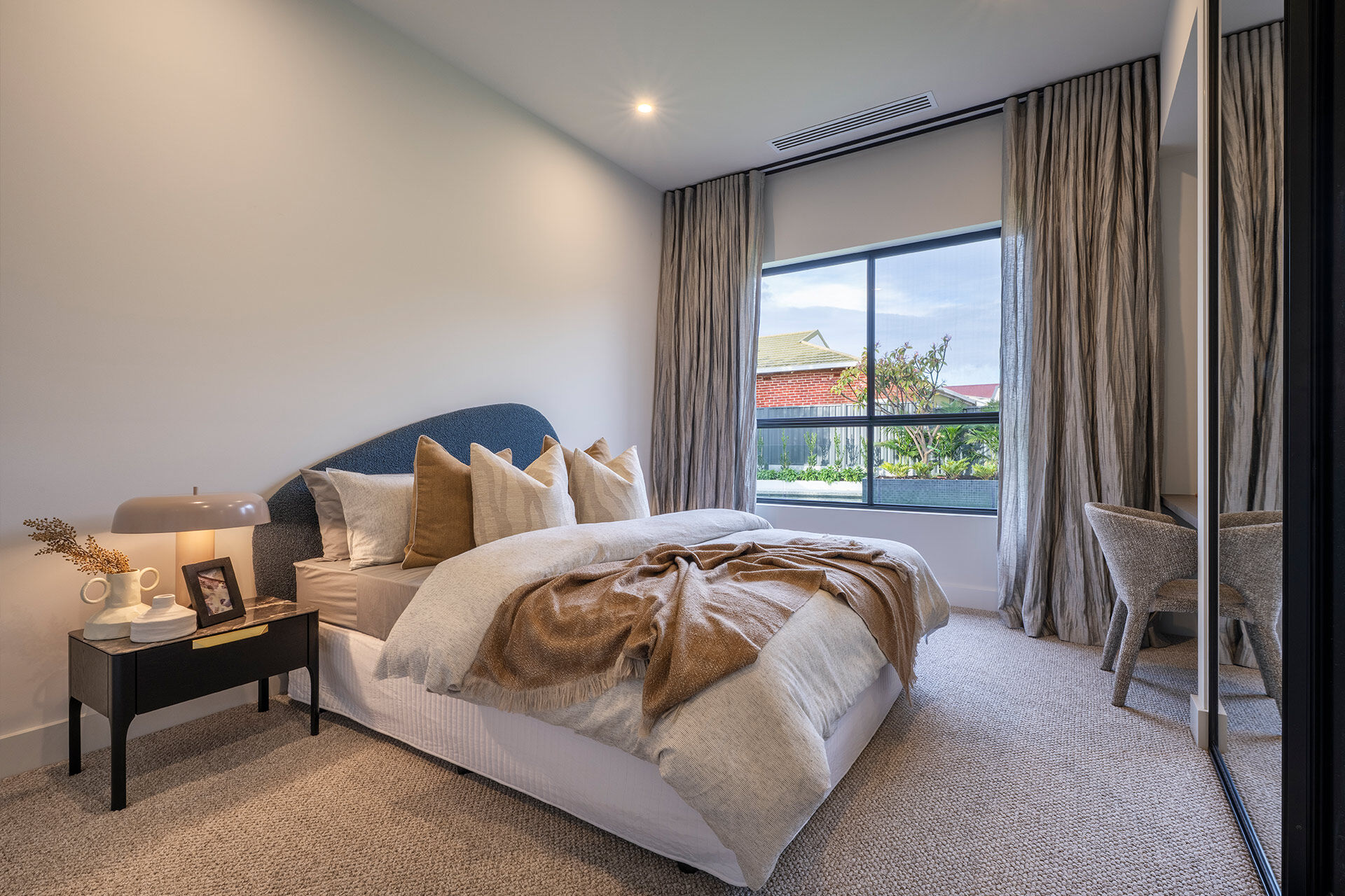 Bedroom with tan and cream bedding and curtains open to the view of the backyard