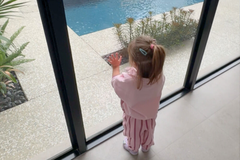 Young girl stands at the window looking out to the pool